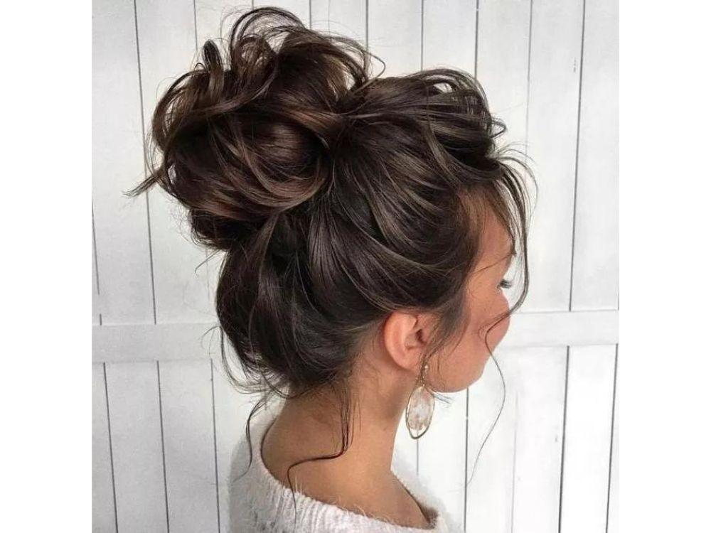 Hoher Messy Bun mit dunklem Haargummi und losen Strähnen